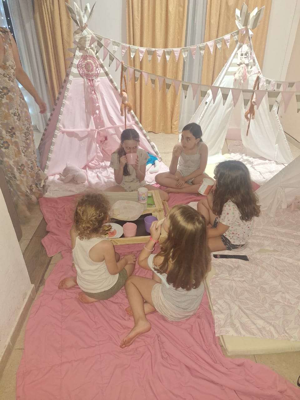 Nenas merendando entre carpas tipi decoradas con atrapasueños y banderines en una pijamada mágica